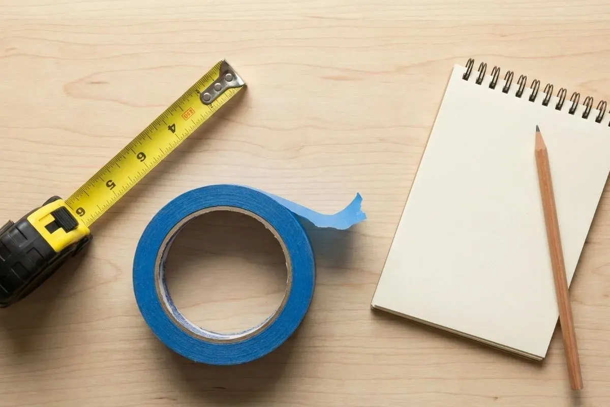 Measuring tape, painter’s tape, and a notepad used to plan a sofa or sectional size